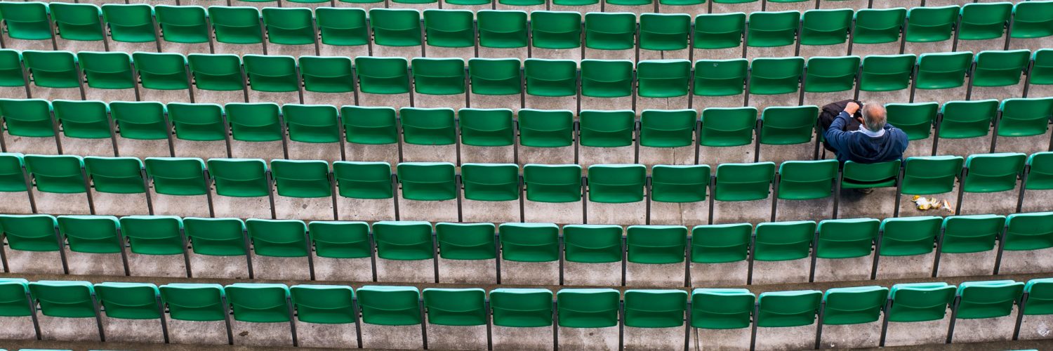 Hundreds of green stadium chairs, one man sitting.