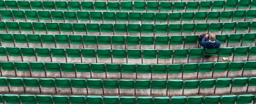 Hundreds of green stadium chairs, one man sitting.