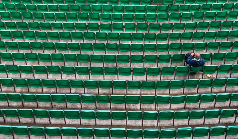 Hundreds of green stadium chairs, one man sitting.